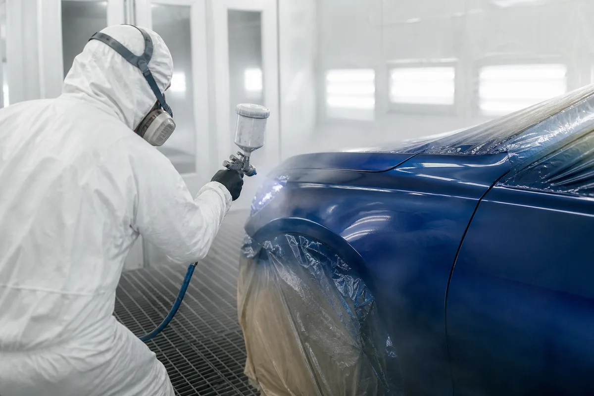 Carrossier appliquant une base au pistolet dans une cabine de peinture éclairée